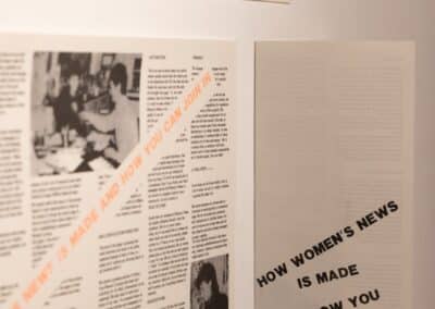 Leaflets featuring text and images displayed on a white wall, two are flat, one is folded. The text in the folded leaflet reads "how women's news is made and how you can join in".