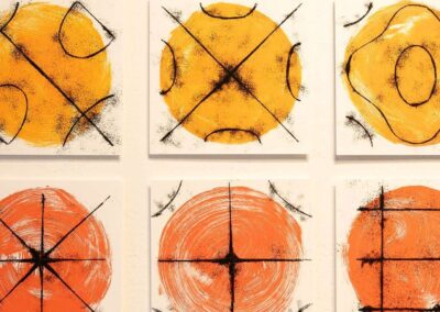 Twelve square prints hung in a grid format. The prints feature yellow, orange, red, and pink circles with black lines and shapes on top.