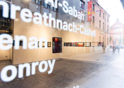 Looking through the window into the gallery space. Lettering on the window and reflection of the street outside are visible.