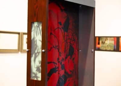 Three dimensional frame box made from burnt and stained pine is suspended from the ceiling. A black and red photo etching is framed in the centre. A green and black screenprint is inlaid behind glass in the side of the frame.