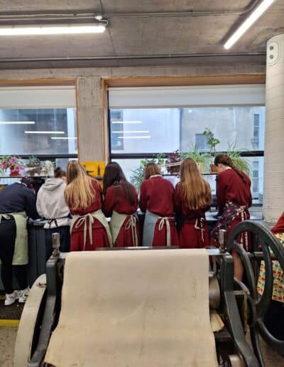 Group of seven school pupils standing in etching workshop, their backs are facing the camera.