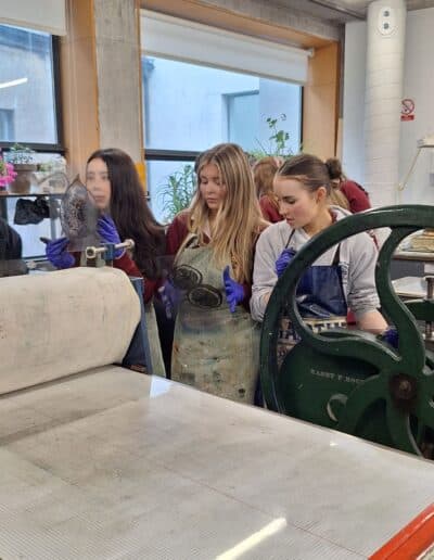 Three school pupils in etching workshop, they are standing beside an etching press and holding acetate drypoint plates.