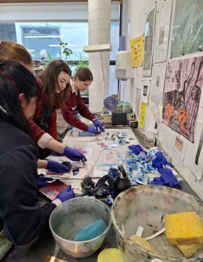 Four school pupils working in etching workshop, they are standing at a bench which has ink, paper, and rags on it.