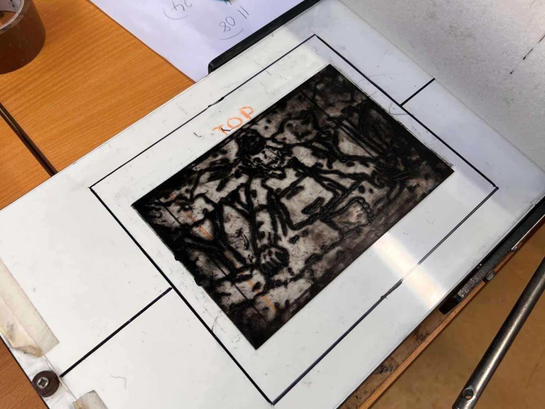 A drypoint plate with black ink on it placed on the bed of an etching press.