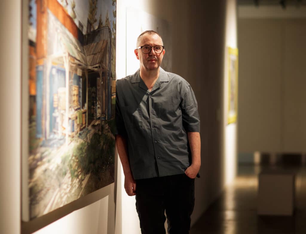 Image of artist Colin Martin alongside one of his paintings in a gallery setting