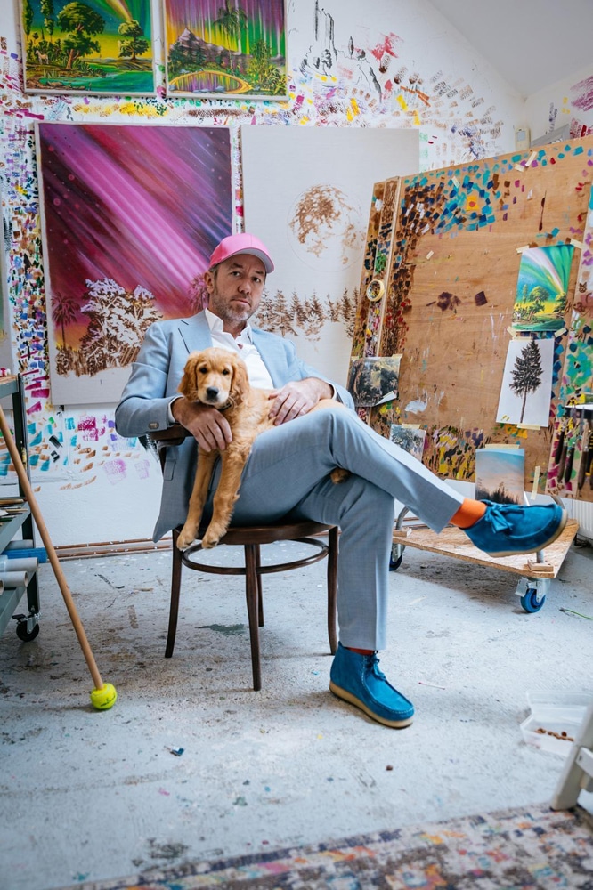 Image of artist with his painting in the background and his dog on his lap